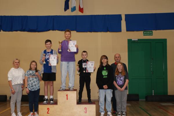 Na podium stoi trzech chłopców z medalami, dyplomami i pucharami.